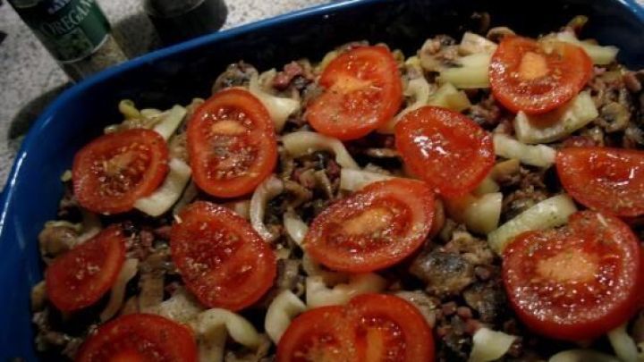Eine bunte Sp&auml;tzle-Pilz-Nudelpfanne liegt in einer blauen Sch&uuml;ssel, belegt mit frischen Tomatenscheiben und Zwiebeln.