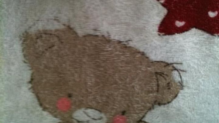 Ein flauschiges Handtuch mit einem niedlichen B&auml;ren, der ein gepunktetes Spielzeug h&auml;lt, im Badezimmer aufgeh&auml;ngt.