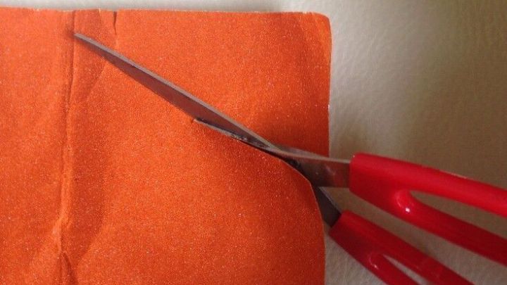 Eine rote Schere schneidet durch einen orangefarbenen Stoff, um stumpfe Scheren wieder scharf zu machen.