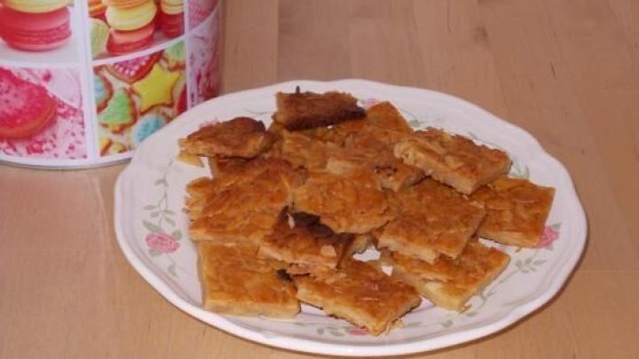 Florentiner liegt gebacken auf einem Teller, flankiert von einer bunten Geb&auml;ckdose auf einem Holztisch.