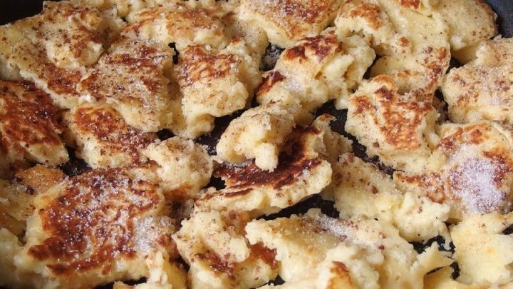 In einer Pfanne liegt ein gebr&auml;untes Quark-Schmarren, das zart zerf&auml;llt, umringt von feinem Zucker und Apfelst&uuml;cken.