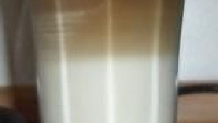 Ein zweifarbiger Latte Macchiato steht auf einem Holztisch. Die Schichten aus Milch und Espresso sind klar getrennt.