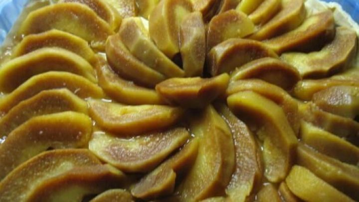 Eine Quitten-Tarte mit goldbraun gebackenen Quittenst&uuml;cken auf einem knusprigen Teigboden, pr&auml;sentiert in einer runden Form.