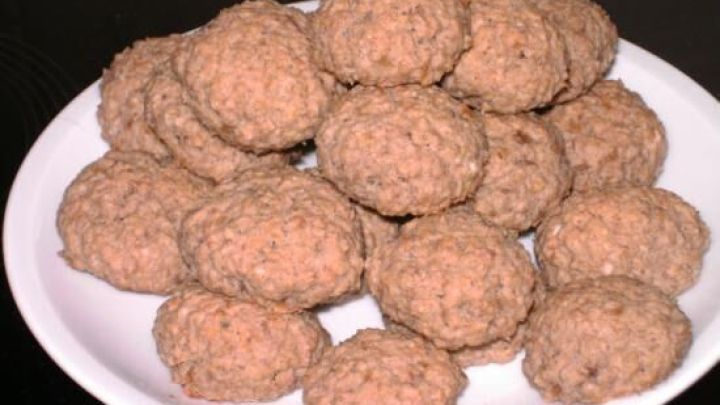 Bananenkekse mit Haferflocken liegen auf einem wei&szlig;en Teller und sind gleichm&auml;&szlig;ig verteilt in einer dunklen Umgebung.