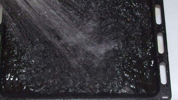 Ein Backblech wird mit Scheuermilch gereinigt, w&auml;hrend Wasser dar&uuml;ber spritzt, um Schmutz zu entfernen.