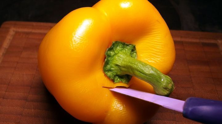 Eine gelbe Paprika wird mit einem lila Messer auf einem Holzbrett geschnitten, um sie frisch zu halten.