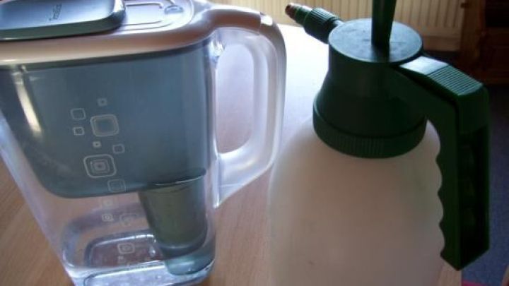 Ein Wasserfilter steht neben einer Spr&uuml;hflasche auf einem Tisch, bereit, Zimmerpflanzen mit gefiltertem Wasser zu versorgen.