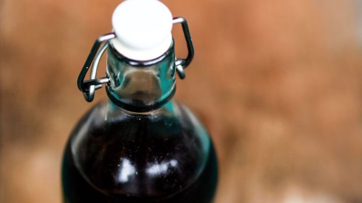 Ein Glasflasche mit verschlossenem Deckel steht auf einem Holztisch, neben ihr liegen einige Olivenzweige und Fr&uuml;chte.