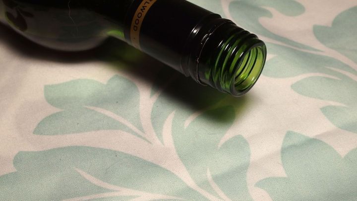 Eine halbleere Flasche Rotwein liegt schr&auml;g auf einer eleganten Tischdecke mit floralem Muster, die unversehrt aussieht.