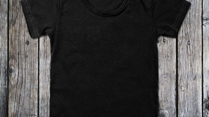 Ein schwarzes T-Shirt liegt auf einer rustikalen Holzoberfl&auml;che und zeigt die zeitlose Mode von schwarzer Kleidung.