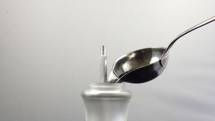 Eine handliche Pfefferm&uuml;hle wird mit einem L&ouml;ffel gef&uuml;llt, w&auml;hrend sie vor einem neutralen Hintergrund steht.