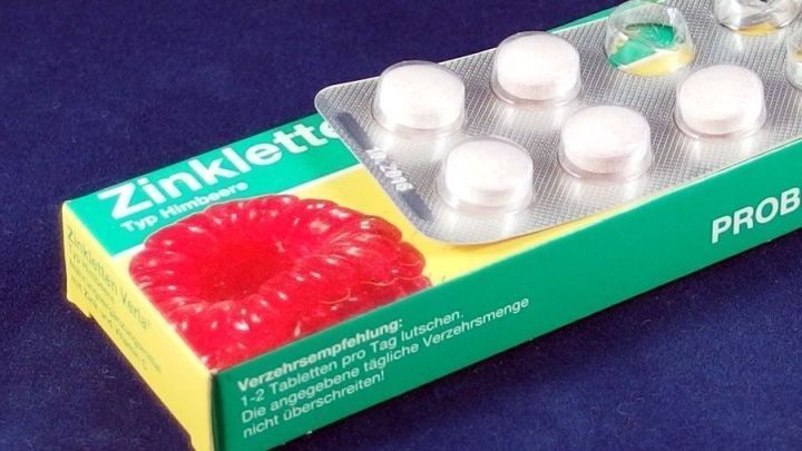 Ein Pillenblister mit mehreren Tabletten liegt auf einer bunten Verpackung. Der Kontext zeigt eine flache, einfarbige Oberfl&auml;che.