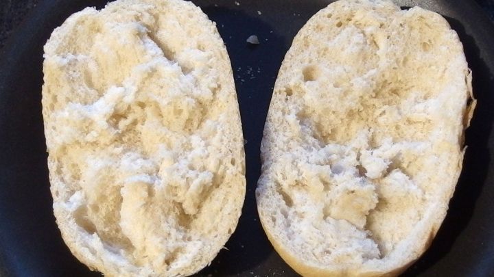 Aufbackbr&ouml;tchen sind aufgeschnitten und zeigen eine trockene, br&ouml;selige Innenseite in einer Pfanne.