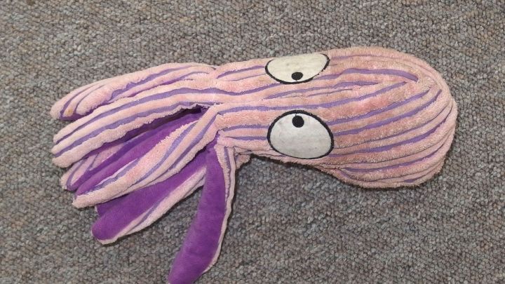 Ein besch&auml;digtes Hundespielzeug in Form eines Oktopus liegt auf einem grauen Teppich. Es erinnert an kreatives Upcycling.