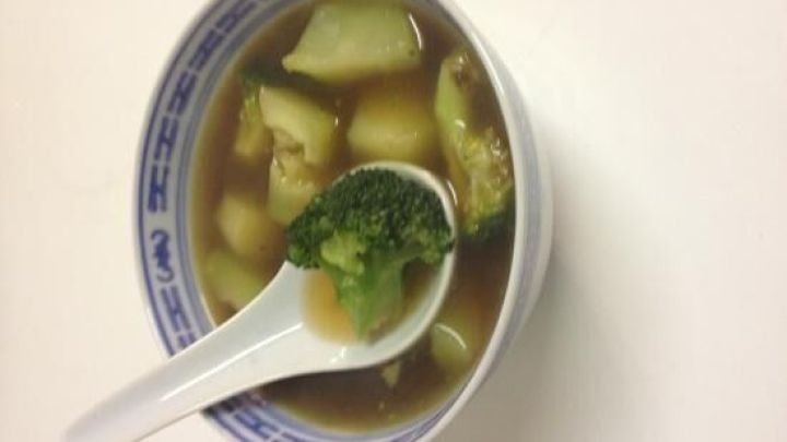 Eine Sch&uuml;ssel Asia-Suppe mit Brokkoli-Strunk und Gem&uuml;se, steht auf einem wei&szlig;en Tisch und wartet auf den Verzehr.