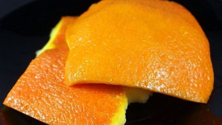 Zwei Orangenschalenst&uuml;cke liegen auf einem schwarzen Teller und sind bereit, Kaugummi zu entfernen.