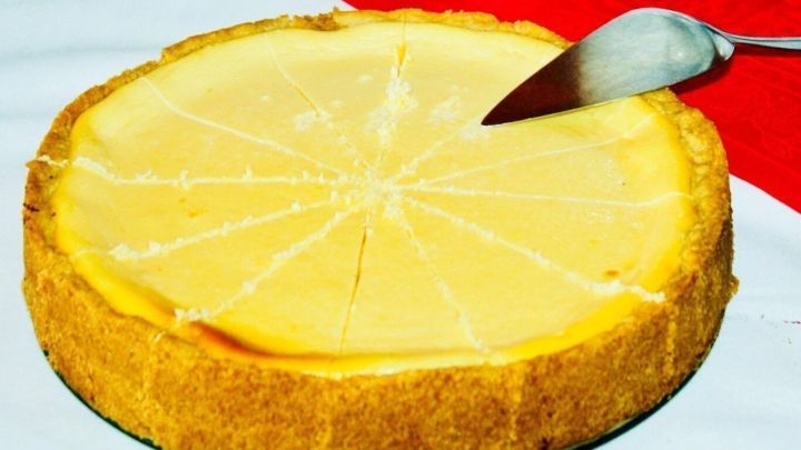 Ein K&auml;sekuchen mit Orangensaft steht auf einem Tisch, w&auml;hrend ein Messer ein St&uuml;ck herausschneidet.