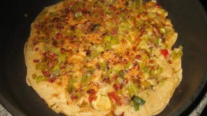 Ein goldbrauner Pfannkuchen mit Lauch und Paprika wird in einer Pfanne gebraten, umgeben von einer gem&uuml;tlichen K&uuml;che.