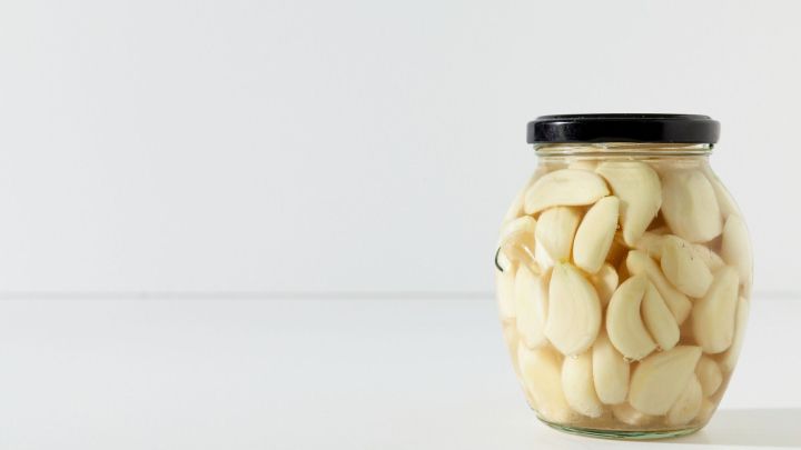 Ein Glas mit eingelegtem Knoblauch pr&auml;sentiert sich vor einem hellen Hintergrund, bereit zum Genie&szlig;en oder Verarbeiten in Knoblauchlik&ouml;r.