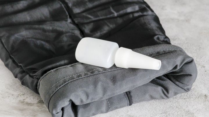 Ein grauer Jacken&auml;rmel liegt flach auf einer Oberfl&auml;che, w&auml;hrend eine Flasche mit Fl&uuml;ssigkeit daneben positioniert ist.