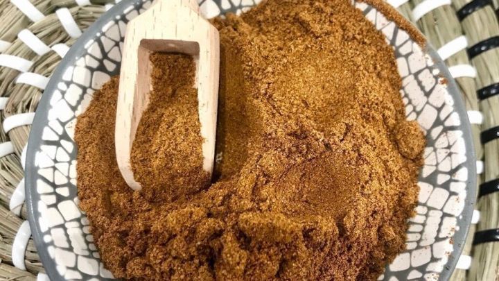 Eine Sch&uuml;ssel mit aromatischer chinesisch-thail&auml;ndischer Gew&uuml;rzmischung und einem Holzl&ouml;ffel auf einem geflochtenen Untersetzer.