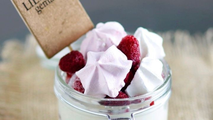 Ein Glas Fr&uuml;chtequark mit Baiser-H&auml;ufchen und Himbeeren steht auf einem Jutesack, beschriftet mit &bdquo;mit LIEBE gemacht&ldquo;.