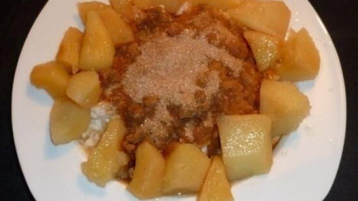 Ged&uuml;nstete Quitten liegen um eine Portion Zimt-Zucker-Milchreis, der auf einem wei&szlig;en Teller angerichtet ist.