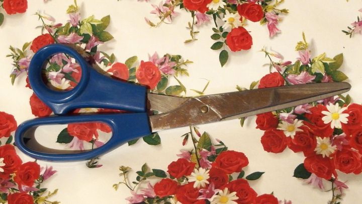 Eine Schere liegt auf buntem Geschenkpapier mit Blumenmustern, bereit, um Reste effektiv zu verwerten und zu schneiden.