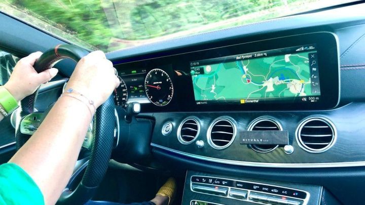 Eine Hand steuert ein modernes Auto, w&auml;hrend das Navigationssystem die Route zur Arbeit anzeigt.