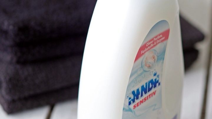 Eine Flasche Weichsp&uuml;ler steht neben einem Stapel dunkler Handt&uuml;cher auf einem Holzuntergrund.