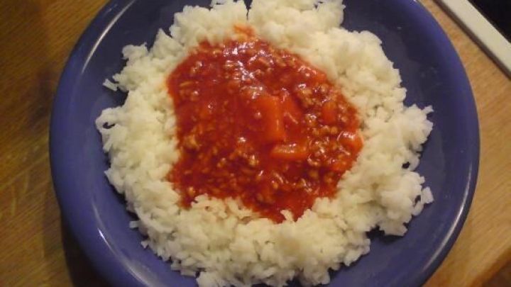 Ein blauer Teller gef&uuml;llt mit wei&szlig;em Reis, der in der Mitte mit einer roten Tomatensauce bedeckt ist, auf einem Holztisch.