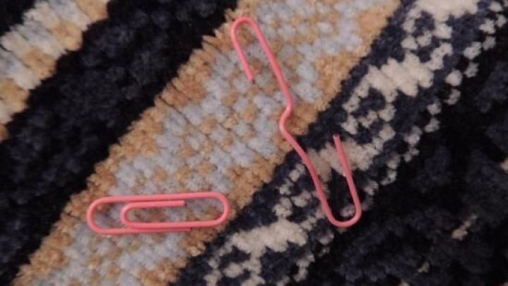 Zwei rote B&uuml;roklammern liegen auf einem gestreiften Pullover, der aus weicher Strickware besteht.