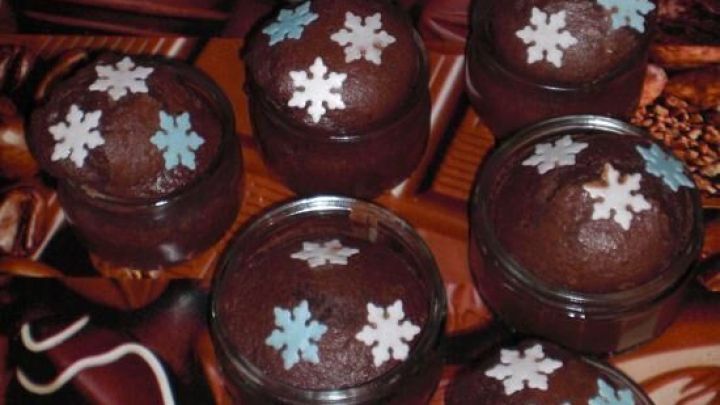Sechs kleine Kuchen aus dem Glas stehen auf einem schokoladigen Hintergrund und sind mit blauen Schneeflocken dekoriert.
