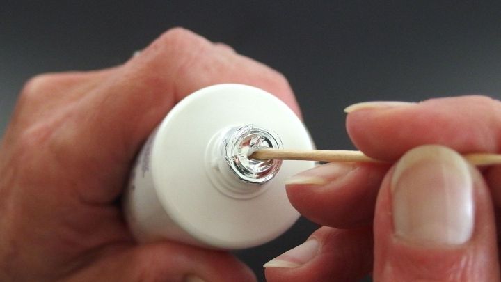 Eine Hand h&auml;lt eine Zahnpastatube, w&auml;hrend ein Holzst&auml;bchen darin gef&uuml;llt wird, um die Dosierung zu optimieren.