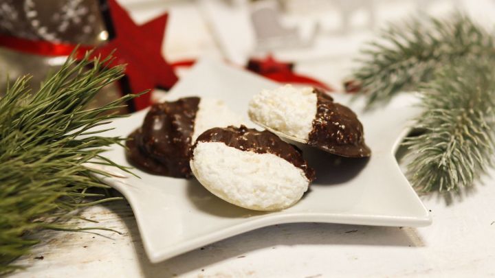 Auf einem Sternteller liegen Kokosmakronen, einige in Schokolade eingetaucht, umgeben von festlicher Dekoration.
