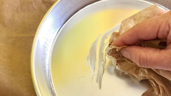 Eine Hand benutzt ein St&uuml;ck Backpapier, um eine fettige Backform zu reinigen, w&auml;hrend sich weiteres Backpapier daneben befindet.