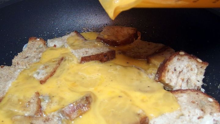 In einer Pfanne liegen gebratene Graubrotscheiben, w&auml;hrend frische Eiermischung dar&uuml;ber gegossen wird.