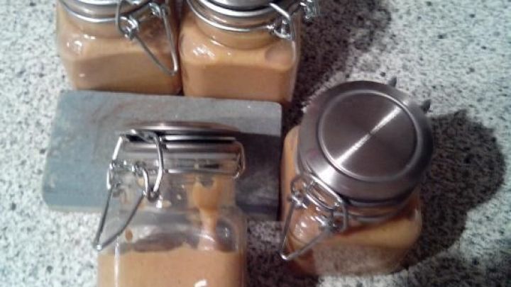 Vier Gl&auml;ser mit selbstgemachtem Honigsenf stehen auf einer grauen Arbeitsfl&auml;che, eines davon ist ge&ouml;ffnet.