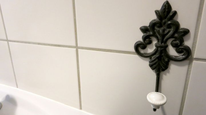 Ein verzierter Haken h&auml;ngt an gl&auml;nzenden Badezimmerfliesen neben einem wei&szlig;en Waschbecken.