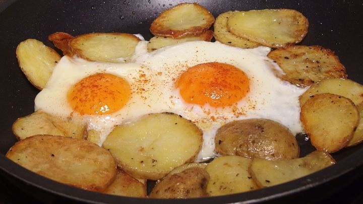In einer Pfanne braten goldene Bratkartoffeln zusammen mit zwei Spiegeleiern, ideal f&uuml;r einen Essensplan f&uuml;r die Woche.