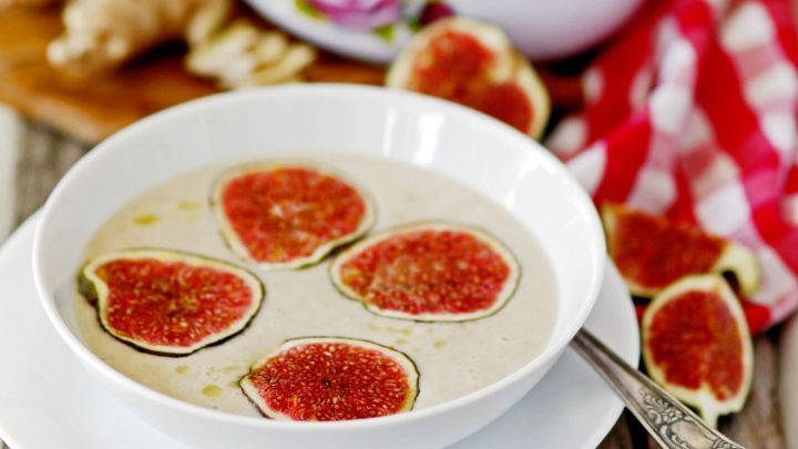 Eine Sch&uuml;ssel Apfel-Feigen-Suppe mit frischen Feigen-Scheiben, umgeben von weiteren Zutaten auf einem rustikalen Holzuntergrund.