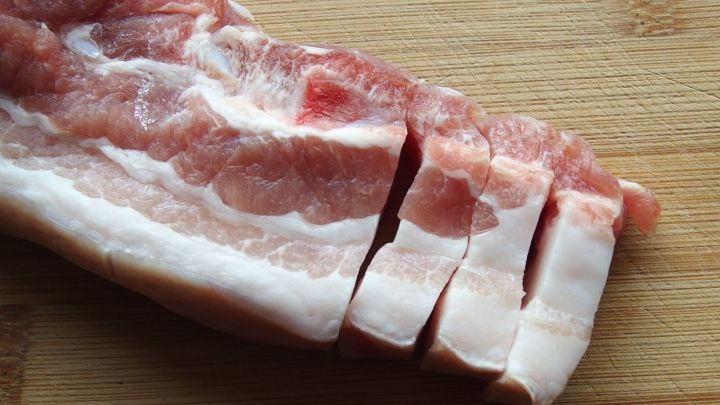 Ein St&uuml;ck Speck ist auf einem Holzbrett in gleichm&auml;&szlig;ige St&uuml;cke geschnitten, wobei die Schnittfl&auml;chen sichtbar sind.