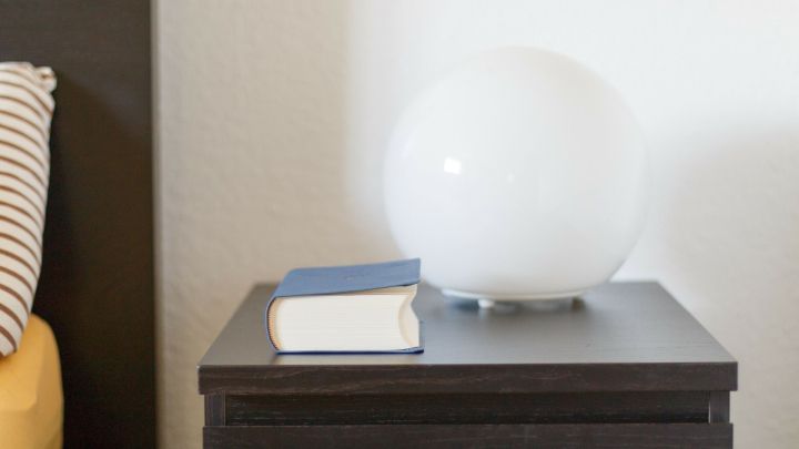Eine runde Lampe steht auf einem Nachttisch neben einem Buch, das f&uuml;r einen besseren Schlaf ohne Elektroger&auml;te sorgt.