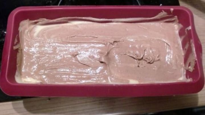 Teig wird in einer roten Kastenform verteilt, bereit zum Backen. Kontext ist eine K&uuml;chenarbeitsplatte.