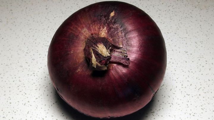 Eine rote Zwiebel liegt auf einer hellen, strukturierten Oberfl&auml;che, bereit zur Verwendung gegen eine verstopfte Nase.