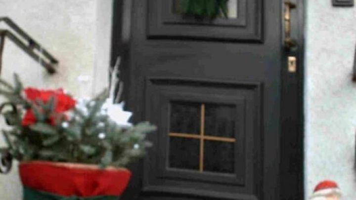 Eine schwarze Eingangst&uuml;r mit einem gr&uuml;nen Kranz und festlicher Dekoration aus roten T&ouml;pfen und einem Weihnachtsmann.