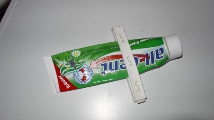 Eine halb leere Plastiktube liegt auf einem Tisch, mit einem Spatel auf ihr, um den Inhalt restlos zu entleeren.