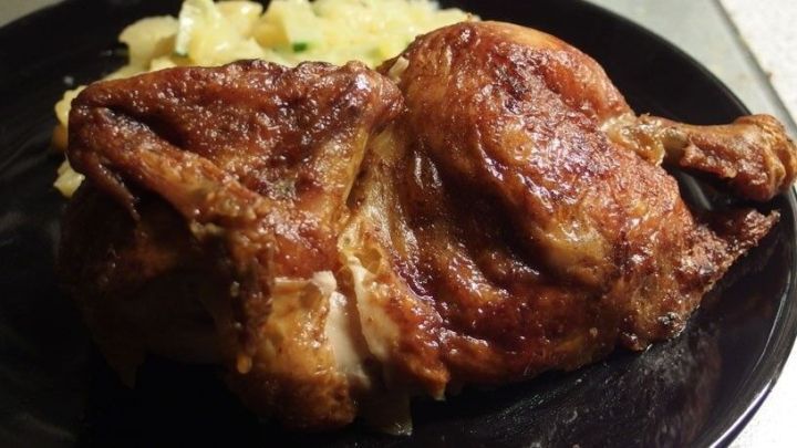 Saftiges, kross gebratenes Gefl&uuml;gel liegt auf einem schwarzen Teller, umgeben von einer Beilage aus Kartoffeln.