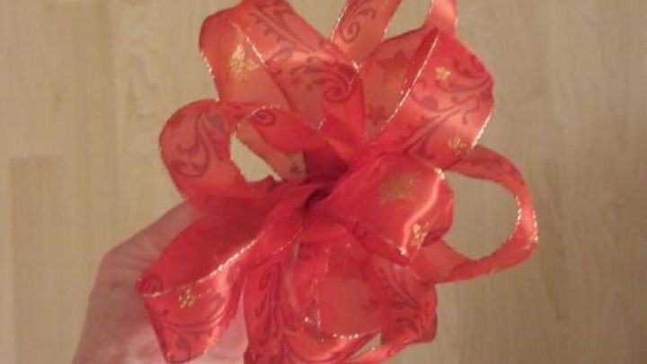 Ein rotes Schleifenband ist in einer Hand gebunden, bereit zum Dekorieren eines Geschenks auf einem hellen Untergrund.