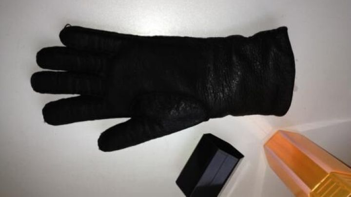 Ein nasser Lederhandschuh liegt auf einem Tisch neben einem kleinen, schwarzen Objekt und einem gelben Flakon.